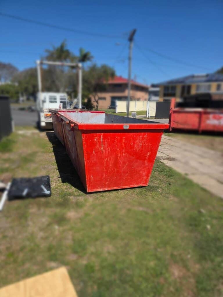 Red Redcliffe Skips skip bins dropped on the grass in Woody Point, next door to Clontarf